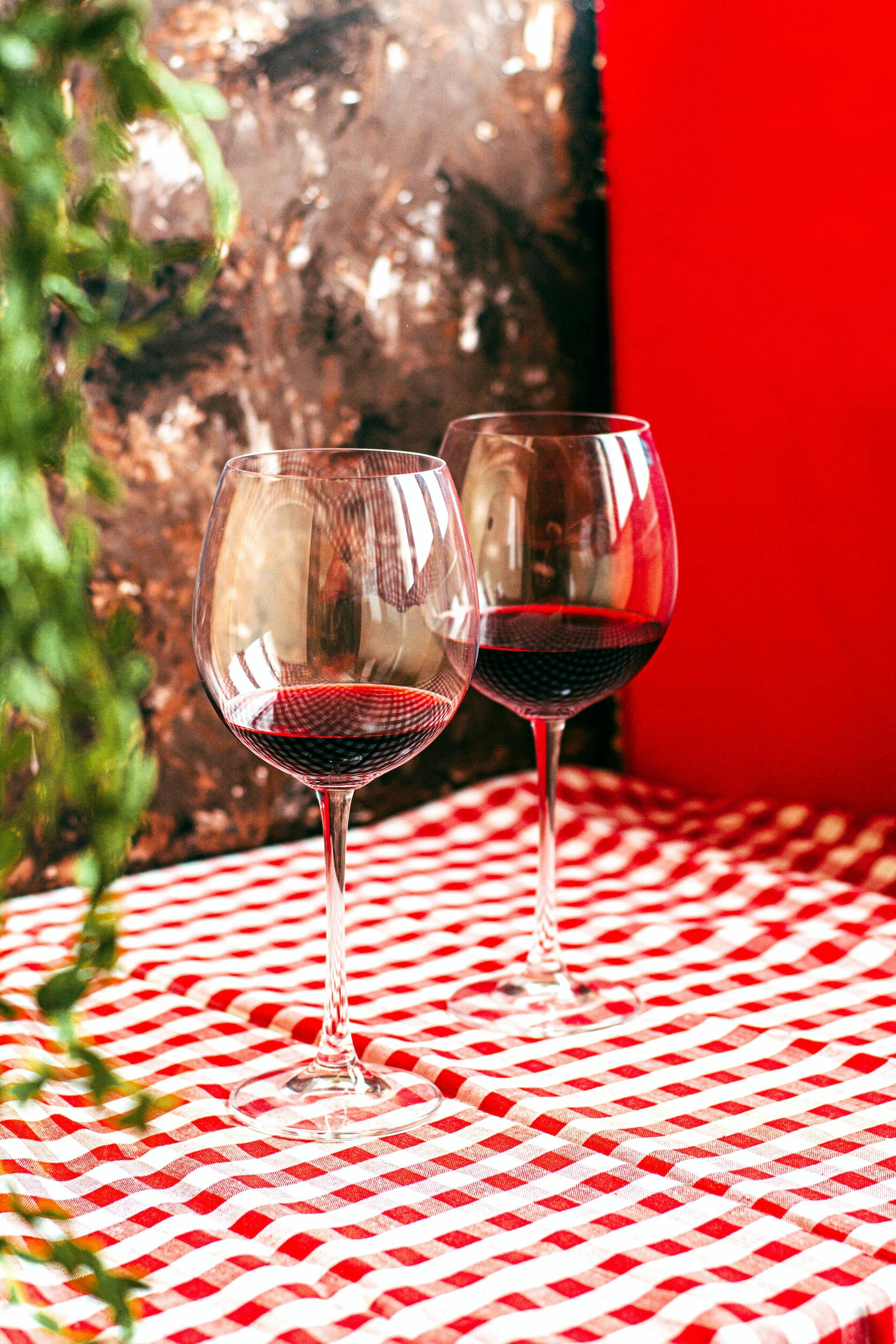 2 Weingläser auf rot-weiß karierter Tischdecke mit roter Flüssigkeit drinnen