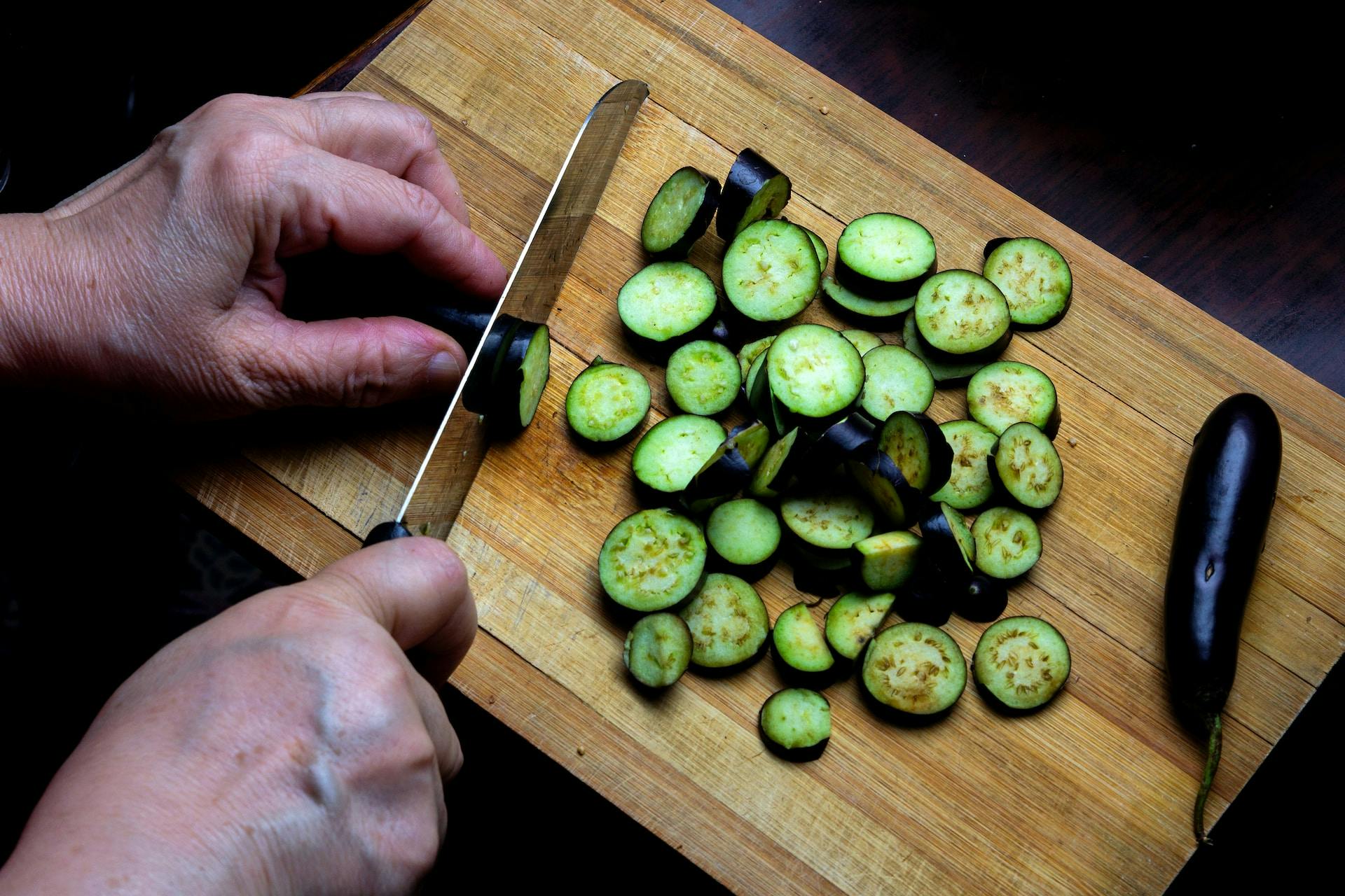 Auf Holzbrett wird Gemüse mit Messer geschnitten
