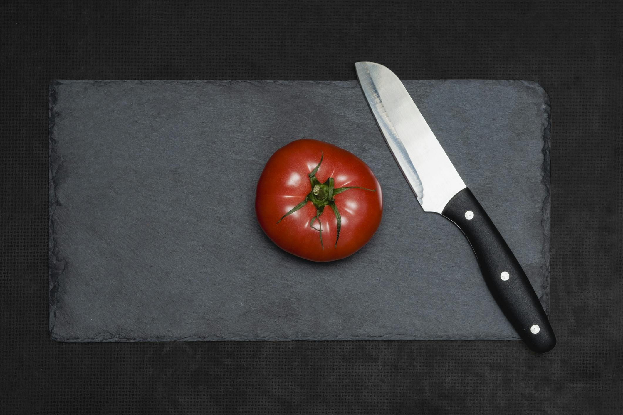 Ein Messer und eine große rote Tomate auf dem Schieferbrett