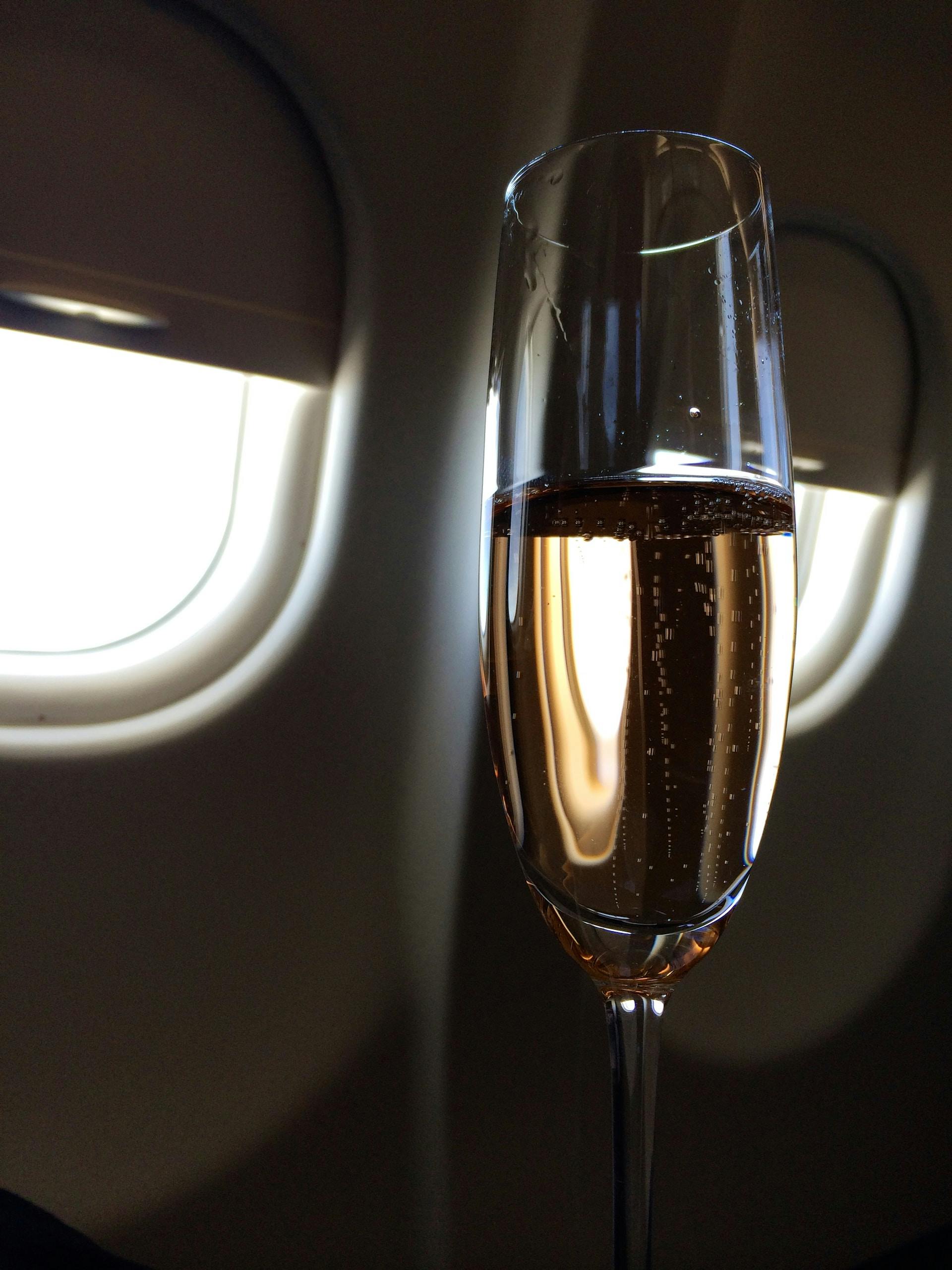 Champagnerglas vor Flugzeugfenster mit gelber FLüssigkeit drinnen