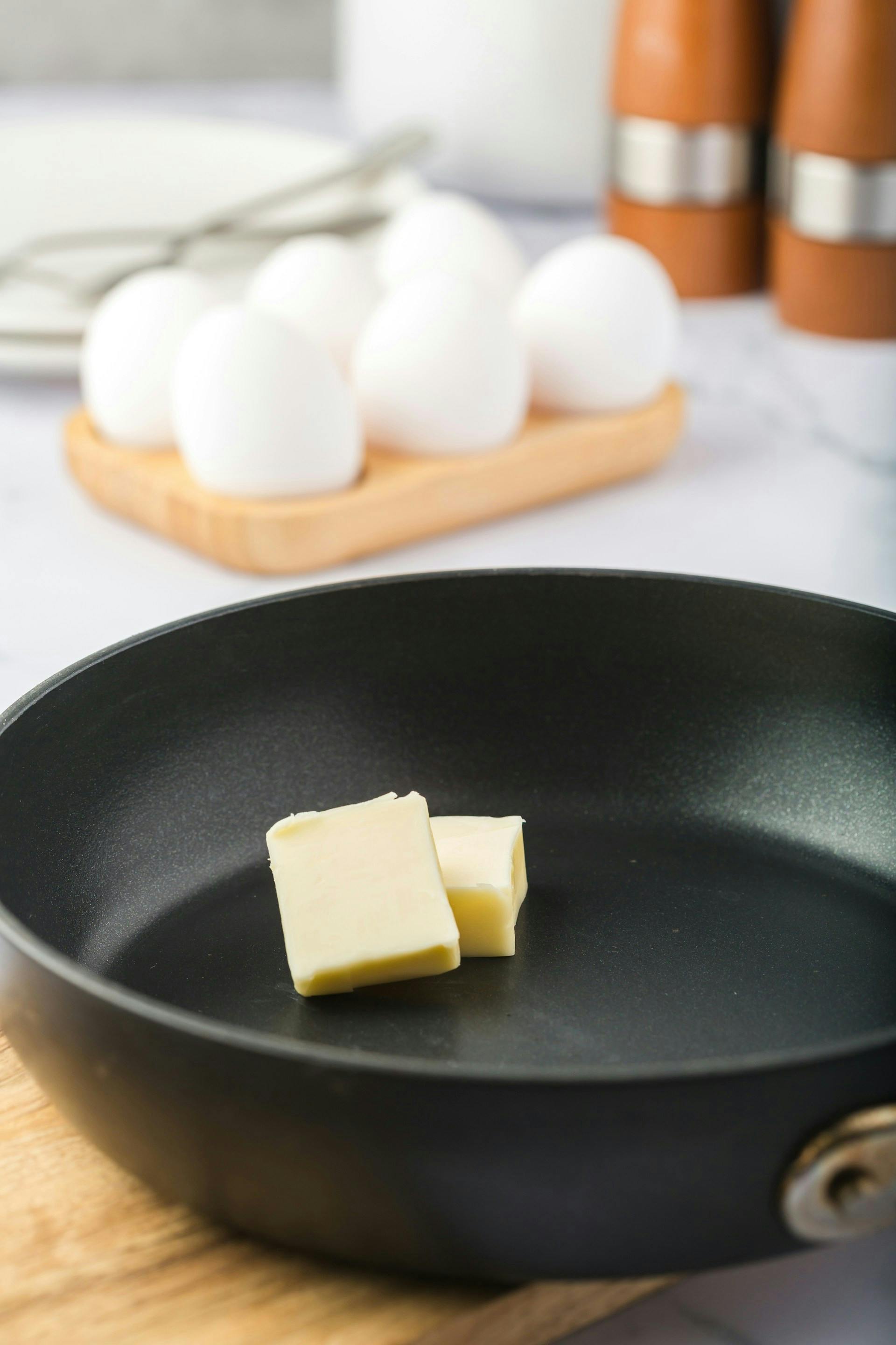 Stück Butter in einer schwarzen Pfanne und Eier auf Küchentisch