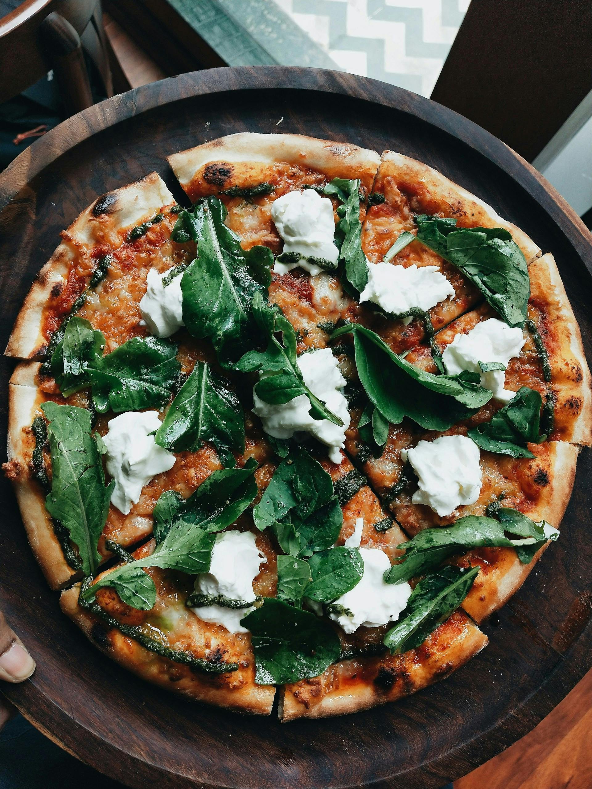 Pizza mit Mozzarella und grünen Blättern drauf auf Holzteller