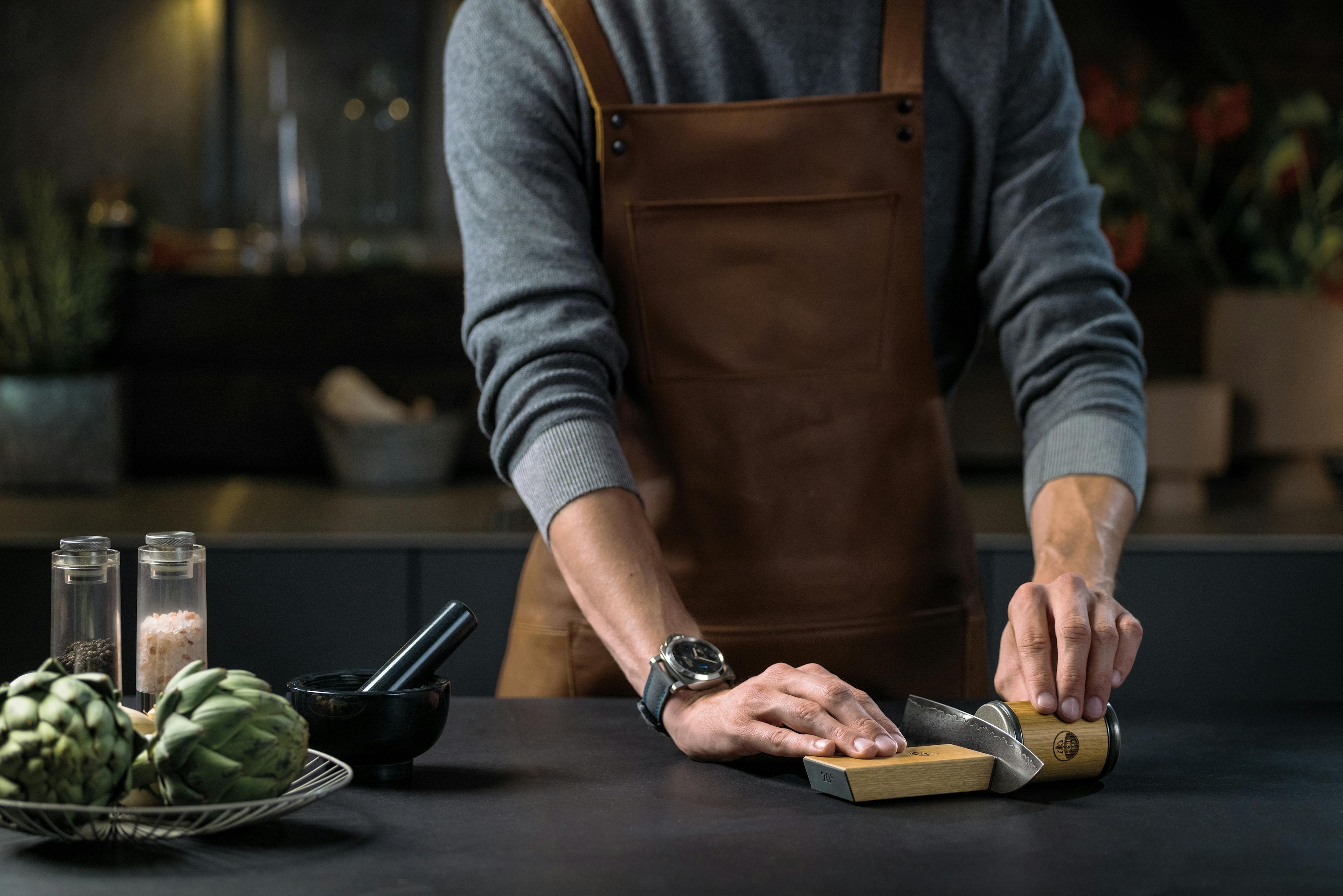 Anwendung eines Messerschärfers von einer Person mit Lederschürze in einer Küche