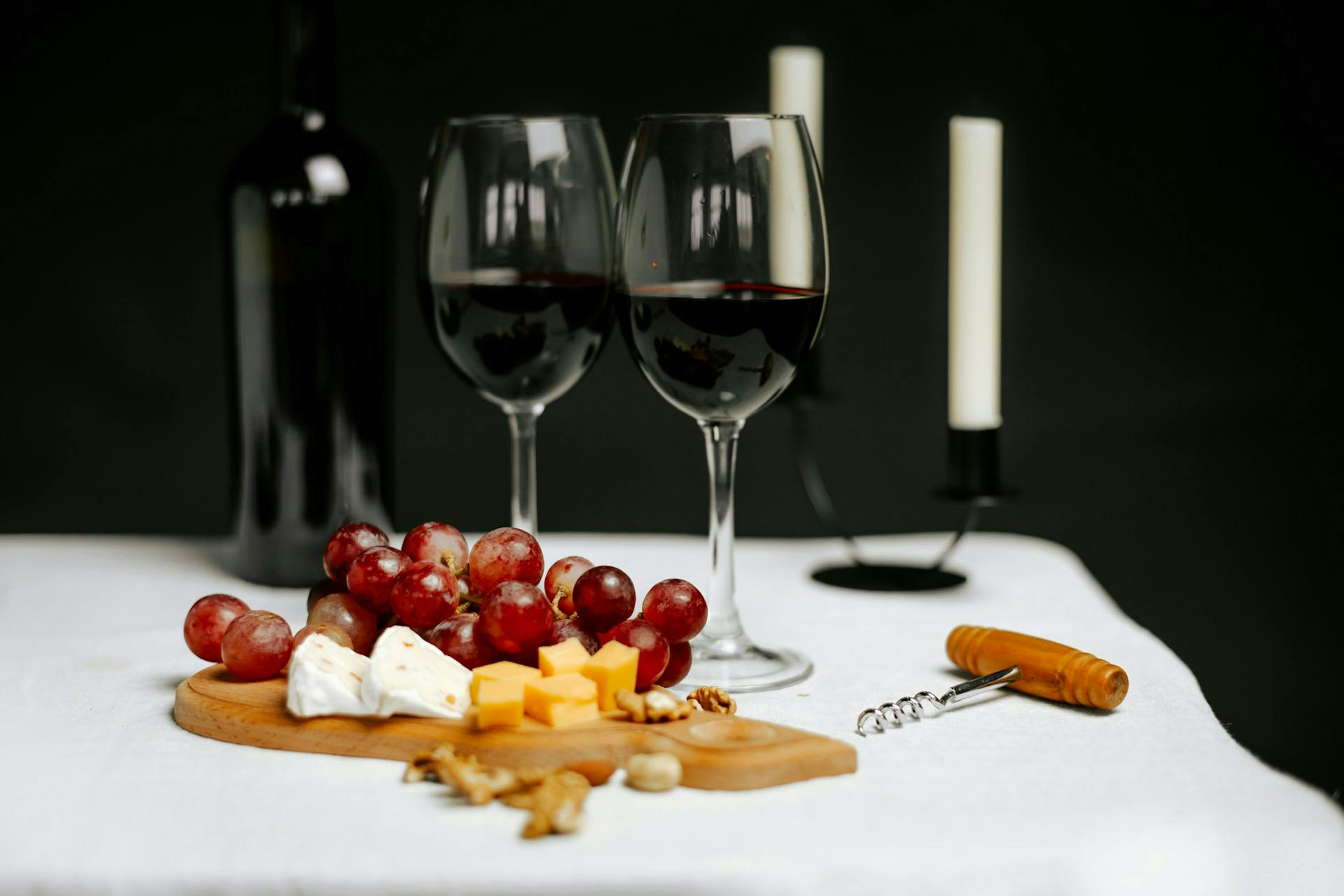 Zwei gefüllte Weingläser stehen vor Holzbrett mit Weintrauben und Käse