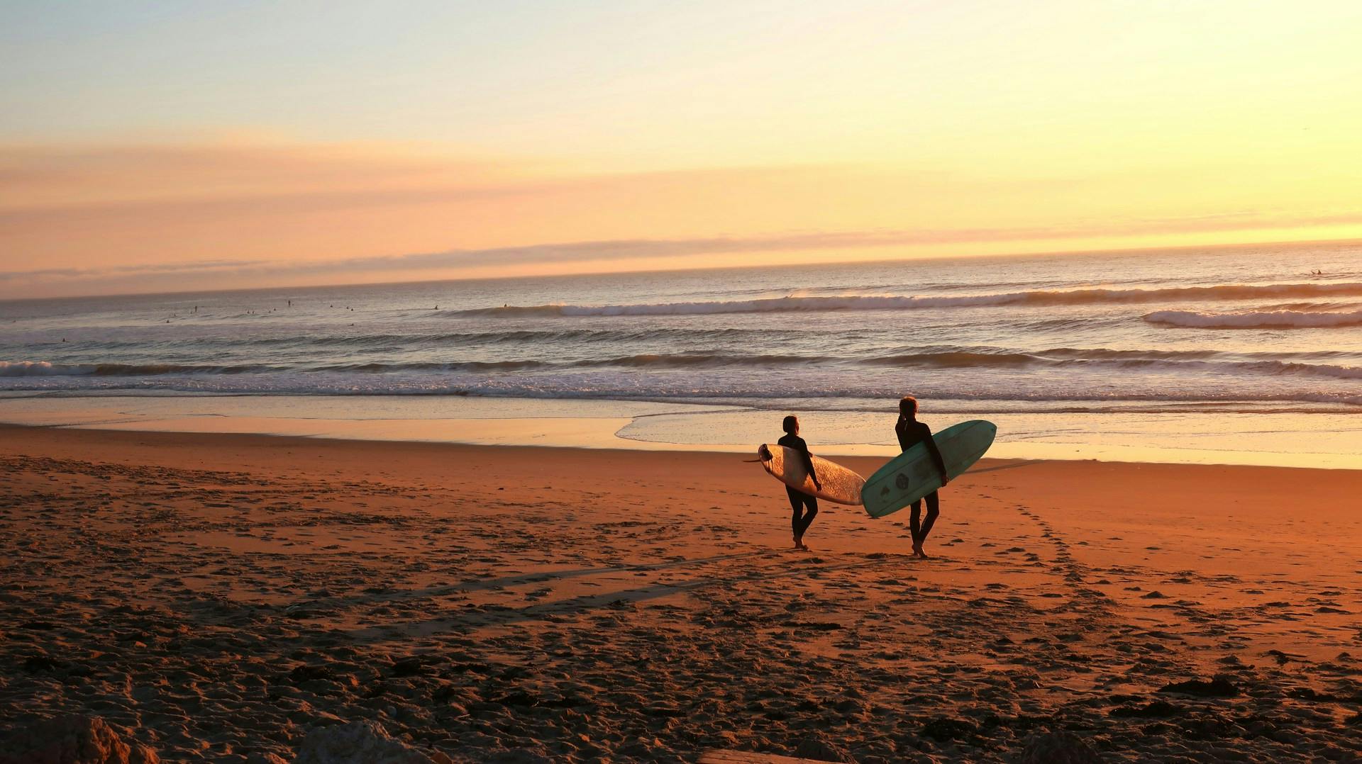 Zwei Surfer spazieren am Strand mit ihren Surfboards. 