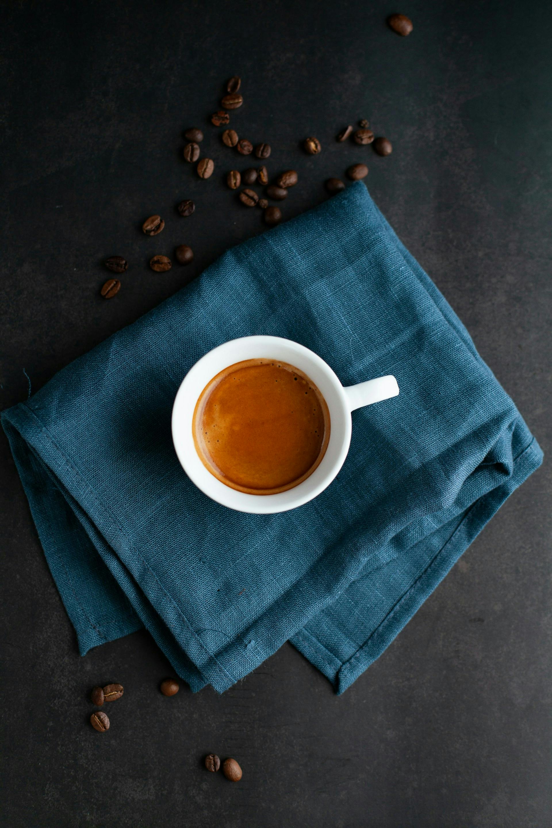Kleine weiße Tasse mit Kaffee steht auf einem blauem Tuch. 