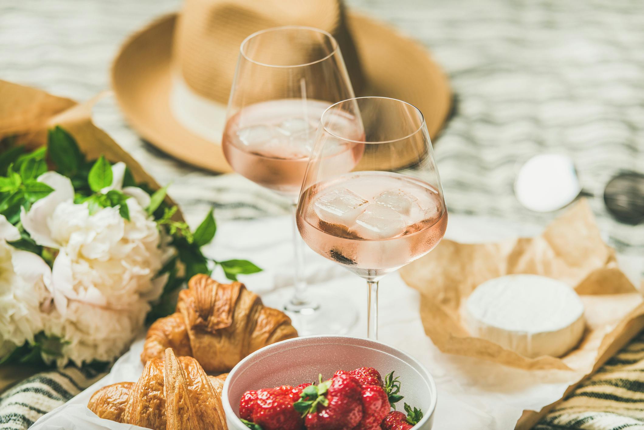 Zwei Gläser mit hellrosa Flüssigkeit umringt von Croissants, Blumen und Erdbeeren